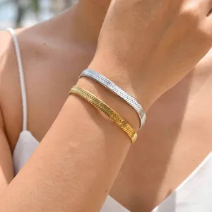 Detail of gold and silver herringbone snake chains layered on wrist with soft outdoor lighting