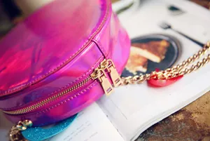 Close-up of pink holographic round crossbody bag with golden chain and zipper details