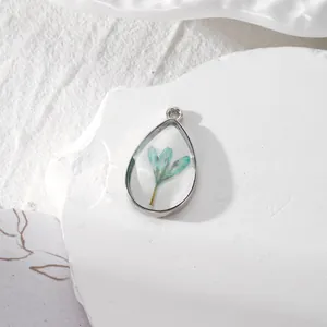 Vue macro du pendentif en résine goutte avec fleurs séchées bleues et cadre en métal argenté