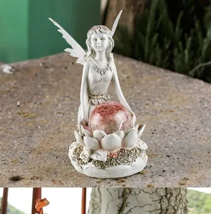 Detail view of fairy statue holding pink cracked glass ball on lotus base in garden