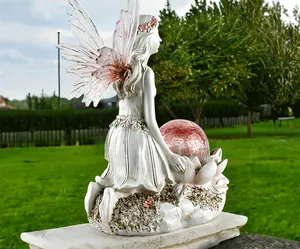 Detail of flower fairy statue with pink crackle glass solar ball on garden grass