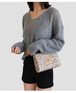 Close-up of a colorful tweed crossbody bag featuring a round gold lock and chain strap