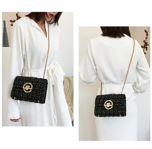 Close-up of black and white tweed chain bag with gold rotary buckle on a white dress
