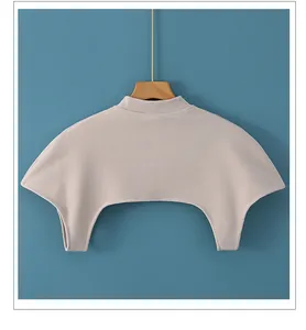 Dettaglio dello scalda-spalle in maglia beige chiaro con collo alto su gruccia