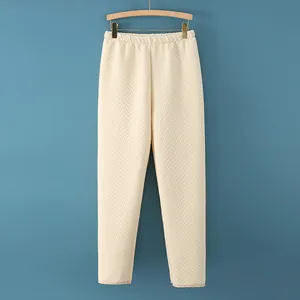Quilted beige thermal trousers for elderly with elastic waist hanging on a wooden hanger
