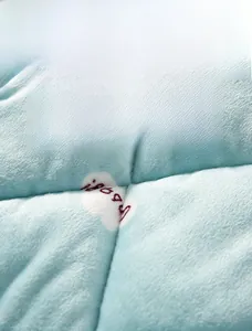 Detailed view of quilted light blue thermal fabric with happy heart embroidery and soft texture