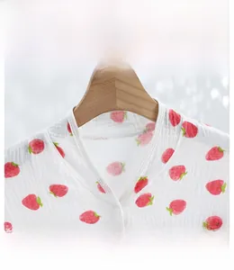 Macro detail of breathable cotton gauze shawl featuring red strawberry print and snap closure