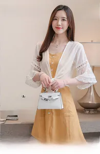Détail d'un cardigan en dentelle blanche avec robe jaune et sac à main en cuir