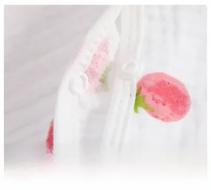 Close-up of strawberry print cotton muslin fabric featuring a small white snap button