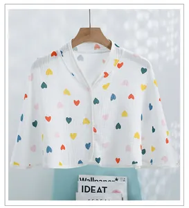 Detail of white cotton gauze shawl with colorful heart print and single button closure