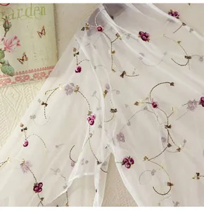 Detail of white mesh fabric featuring delicate red floral embroidery and golden stems