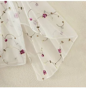 Detail of white sheer mesh fabric with purple flower and brown vine embroidery