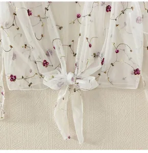 Close-up of white sheer mesh cardigan with floral embroidery and bow tie closure detail