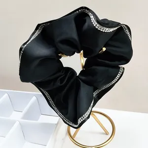 Elegant black satin hair scrunchie with sparkling rhinestone edges on a gold stand