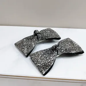 Detail shot of two bow-shaped hair clips with sparkling rhinestones on marble surface