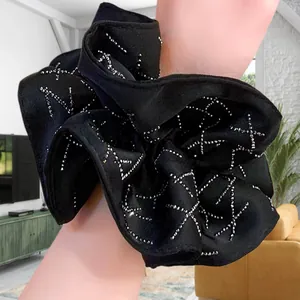 Elegant large black satin scrunchie with rhinestones worn on a wrist in a cozy room