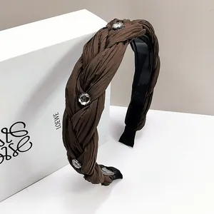 Detail eines dunkelbraunen geflochtenen Stoff-Stirnbands mit glitzernden Strasssteinen