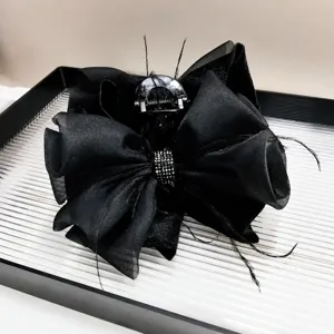Detail of 13cm black bow claw clip with rhinestones and feathers on a striped tray