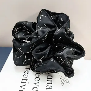 Macro detail of black satin scrunchie with silver sequin X-pattern and elegant folds