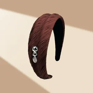 Dettaglio fascia per capelli in tessuto marrone a pieghe con strass e targhetta SMILE