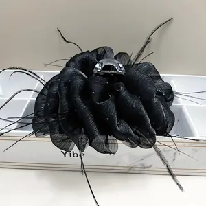 Detail of black cloud tulle hair claw clip with feather accents and sequins on marble box