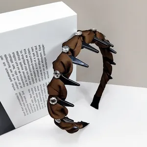Detail of brown pleated fabric headband with black spikes and sparkling rhinestones