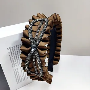 Close-up of brown pleated satin headband with rhinestone bow and crystal detailing