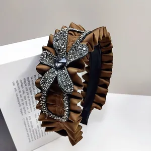 Detailed view of brown satin pleated headband with a sparkling rhinestone flower motif