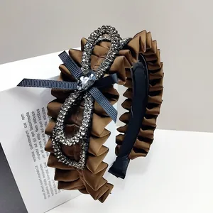 Detail of pleated brown satin headband featuring a rhinestone bow and crystal drop