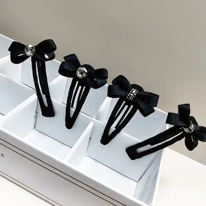 Detailansicht von vier schwarzen Schleifen-Haarspangen mit Kristallakzenten in einer Box