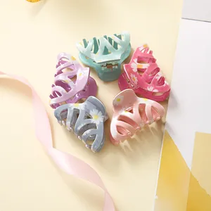 Close-up of five colorful daisy hair claws in mint, pink, lilac, and blue on yellow