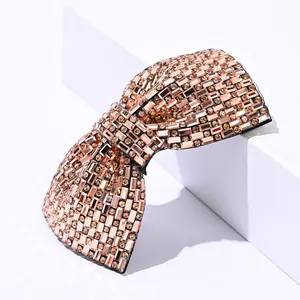 Detailed close-up of champagne crystal bow hair clip with sparkling rhinestones on white stand