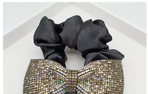 Dettaglio di uno scrunchie in raso nero con un grande fiocco decorato da strass colorati