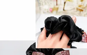 Dettaglio macro dello scrunchie in raso nero con fiocco di strass rosa sfumati