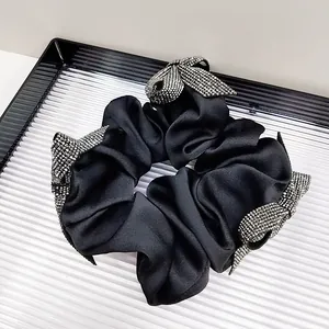 Close-up of black satin scrunchie with sparkling rhinestone bow knots and premium texture