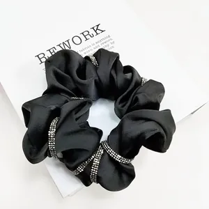 Detail of luxury black satin scrunchie with sparkling rhinestone chain and soft fabric folds