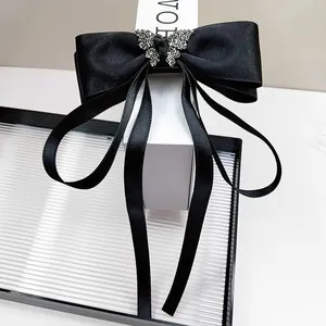 Detail of a black satin bow hair clip with a sparkling rhinestone butterfly and long ribbons