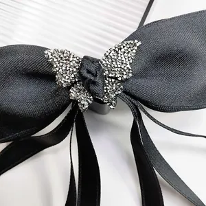 Detail of a black satin bow hairclip featuring a sparkling rhinestone butterfly ornament