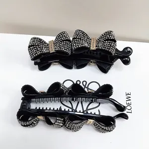 Detail showing two black bow banana hair clips with sparkling rhinestones and metal buckle