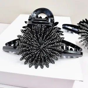Detail of sunflower hair claw clip with silver rhinestones on polished black resin surface