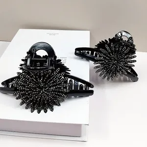 Detail of two black sunflower hair claws with sparkling rhinestones in a white gift box