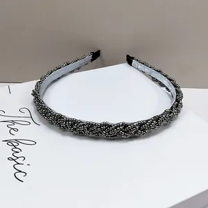 Detalle de la diadema trenzada con cuentas gris oscuro y diseño ondulado metálico
