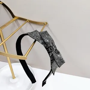 Detail shot of a black thin headband featuring a large bow fully encrusted with sparkling rhinestones