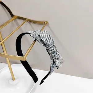 Detailed view of a black headband featuring a sparkling silver rhinestone bow on a gold stand