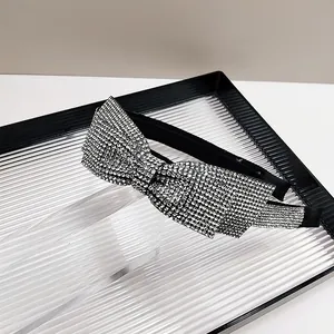 Detailed close-up of a sparkling silver rhinestone bow headband on a black fabric base