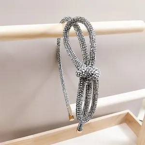 Elegant silver rhinestone headband with knotted bow design on a minimalist wooden stand