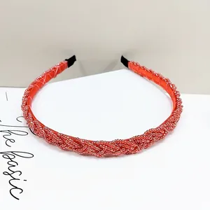 Detalle de diadema trenzada de cuentas rojas con textura brillante y puntas de tela