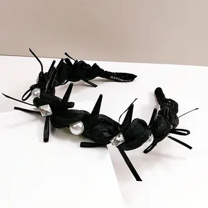 Gothic black wavy headband with rhinestones, pearls, and spikes on a white surface