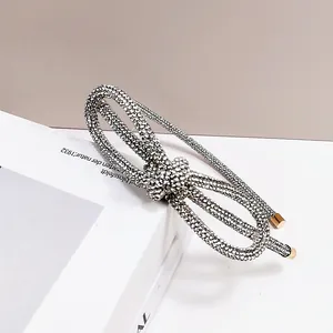 Detail of a thin rhinestone headband with a sparkling double-layered bow and gold tips