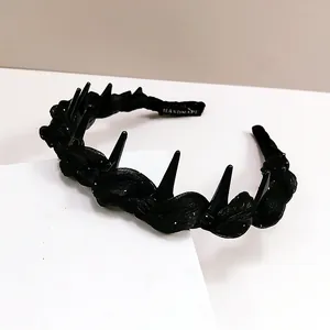 Close-up of black punk headband with spikes and handmade label on white display stand